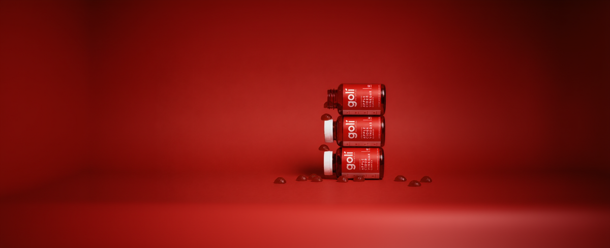 Three red bottles of golf tees stacked vertically on a red studio background, with a few glossy teedrops scattered around them. The label shows the brand name 'golf tees'.