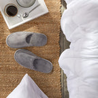 Bulk pack of twelve pairs of individually wrapped gray spa slippers arranged neatly for hospitality use.